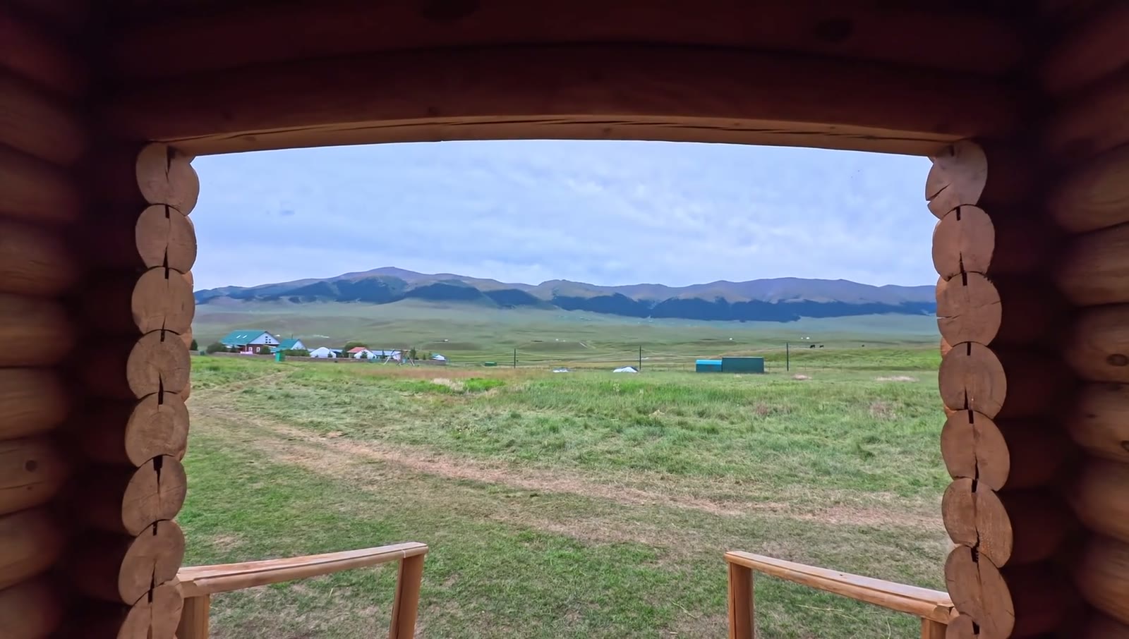A wide green valley and distant mountains viewed through a log cabin doorway